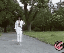 a woman in a white jacket and white pants walking down a path