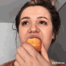 a woman with a nose ring is eating a fried food item