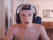 a shirtless man wearing headphones and a hat is sitting in front of a computer screen .