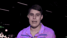 a young man wearing a purple shirt and a hat is smiling in front of a black background .