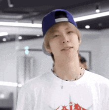 a young man wearing a white t-shirt and a blue hat is looking at the camera .