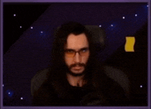 a man with long hair and glasses is sitting in front of a microphone in a dark room .