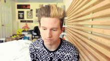 a young man wearing a black and white sweater is sitting in front of a wooden wall