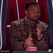 a man in a camouflage jacket is sitting at a table with a nbc logo in the corner