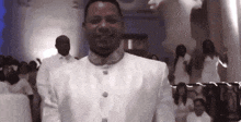a man in a white suit stands in front of a crowd