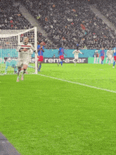 soccer players on a field with a rent-a-car advertisement in the background
