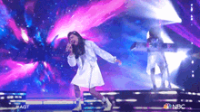 a girl singing on a stage with a nbc logo in the background