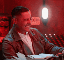 a man in a leather jacket is smiling while sitting at a table in front of a sign that says ech