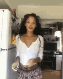 a woman in a white top is dancing in front of a refrigerator