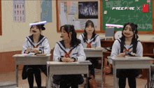 a group of girls sit at desks in front of a blackboard that says free fire
