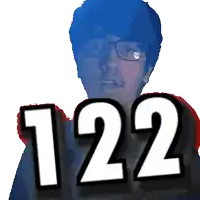 a man with glasses holds up the number 122 in front of his face