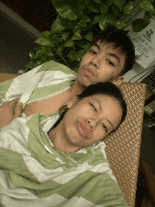 a man and a woman are laying on a wicker chair with a sign behind them that says no smoking