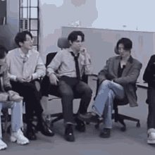 a group of people are sitting in chairs in a room and talking to each other .