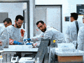 a group of men in lab coats and gloves are working on a table