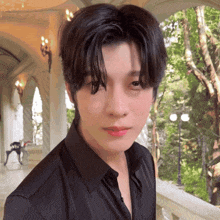 a young man in a black shirt is looking at the camera with trees in the background