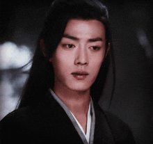 a young man with long black hair is wearing a black jacket and a white shirt .