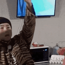 a man is sitting in front of a microwave and a television while raising his arm in the air .