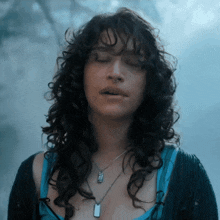 a woman with curly hair wearing a necklace with a dog tag on it