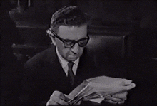 a man wearing glasses is reading a book in black and white