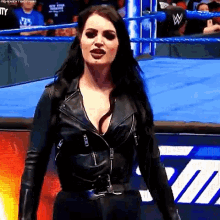 a woman is standing in a wrestling ring wearing a black leather jacket and black pants .