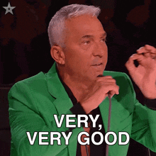a man in a green jacket holds a microphone and says very very good