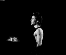 a black and white photo of a man without a shirt on standing in the dark .