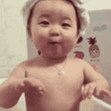 a baby with a towel on his head is standing in a bathtub and looking at the camera .