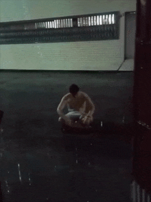 a shirtless man sits in a dark room with a window