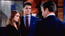 a man in a suit stands next to a woman and a man in a suit and tie