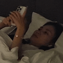 a woman is laying in bed looking at a cell phone .