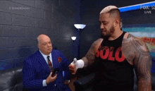a man in a suit and tie is talking to another man in a room while holding a remote control .