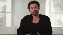 a man with a beard is sitting at a table with his eyes closed and making a funny face .