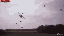 a plane with parachutes is flying over a field with gifs.com written on the bottom right