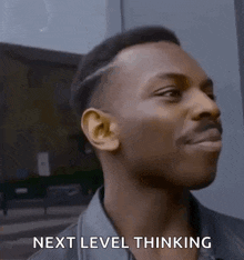 a man is smiling and saying `` next level thinking '' while standing in front of a building .