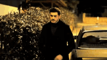 a man in a black coat is standing in front of a car .