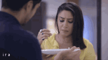 a woman in a yellow shirt is looking at a man holding a plate of food