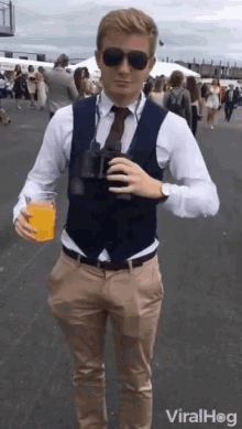 a man wearing a vest and tie is holding a glass of orange juice and binoculars .
