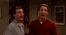 two men are standing next to each other in a room laughing .