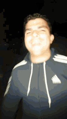 a man wearing a blue adidas jacket is smiling