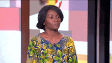 a woman wearing a colorful shirt stands in front of a colorful background