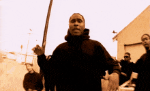 a man in a black hoodie holds a sword in front of a group of men