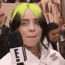 billie eilish is holding a microphone in front of her face .