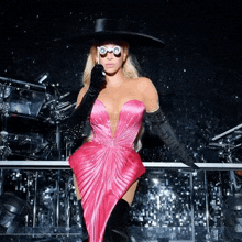 a woman in a pink dress and black gloves is wearing a black hat