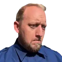 a bald man with a beard wearing a blue shirt looks at the camera