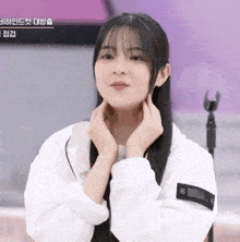 a young woman in a white jacket holds her hands to her chin