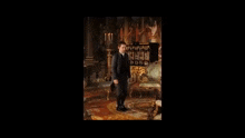 a man in a suit is standing in a living room with a couch .