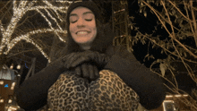 a woman wearing leopard print pants and a supreme hat smiles