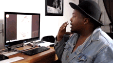 a man wearing a hat is sitting in front of a computer with a picture of a man on the screen