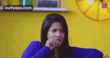 a woman in a blue sweater is sitting on a blue couch and eating a candy bar .