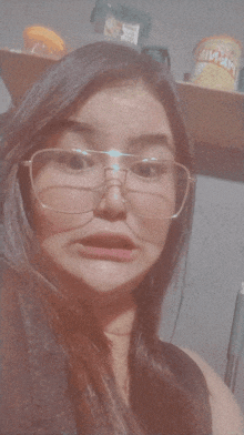 a woman wearing glasses is making a funny face in front of a shelf that has a can of fritos on it